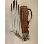 A vintage leather golf club bag by Spalding together with a collection of vintage woods, putters and