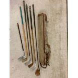 A vintage canvas and leather pencil golf club bag with a small collection of vintage golf clubs to