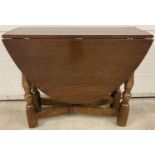 A chunky legged mid century oak drop leaf table with oval shaped top and gate leg supports.