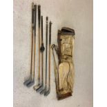 A vintage canvas and leather pencil golf club bag together with 6 vintage golf clubs in varying
