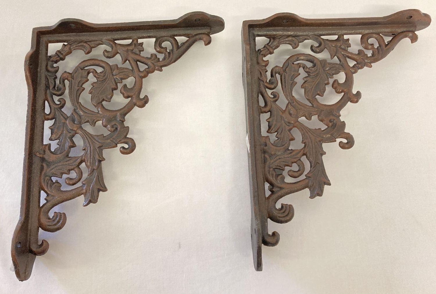 A pair of rust effect cast metal wall shelf bracelets, with decorative scroll & leaf design. Approx.