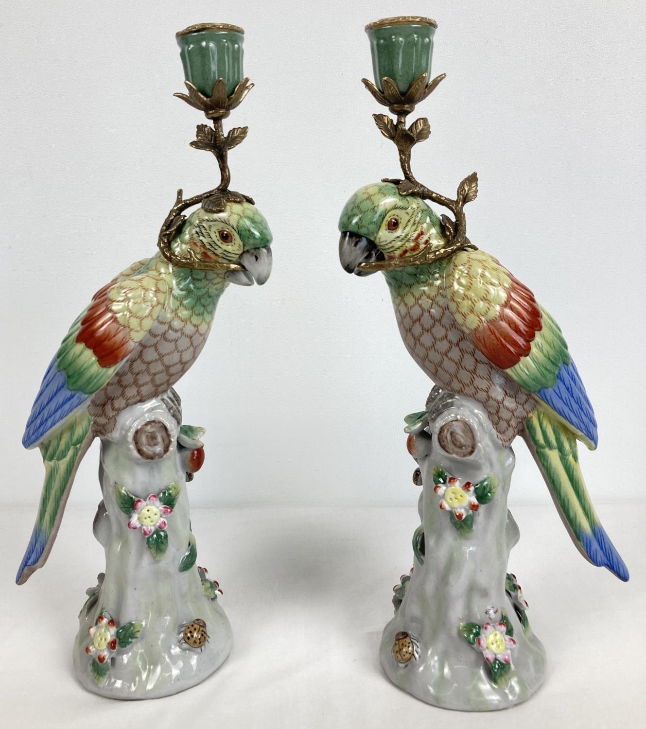 A pair of ceramic candlesticks modelled as parrots sitting atop a stump. With flower and insect