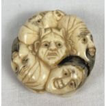 A bone netsuke carved in the form of 9 different faces. With slits to side panels and central hole