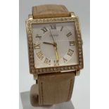 A ladies Guess wristwatch with nude leather strap. Square gold tone case set with clear crystal