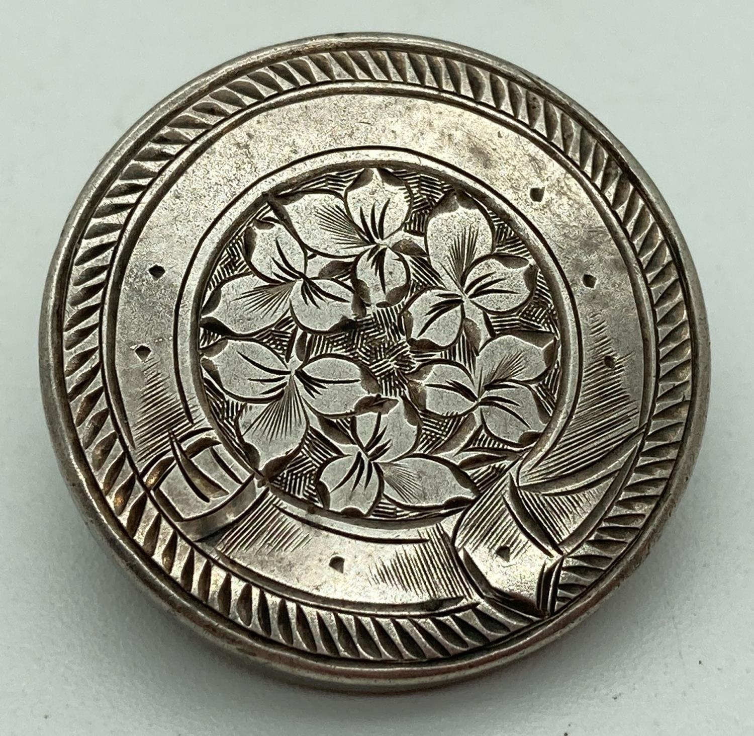 A vintage silver pin back brooch with floral detail framed with engraved belt decoration. Approx.