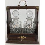 A vintage dark wood tantalus housing a pair of cut crystal square shaped decanters with ceramic