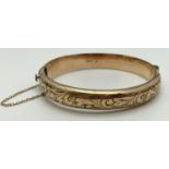 A vintage rolled gold bangle with safety chain, push clasp and half engraved floral decoration.