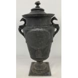 A vintage cast metal lidded urn with horse and rider decorated panel to front and back, floral