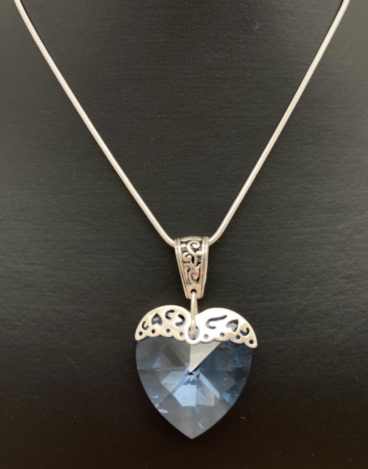 A large pale blue crystal heart shaped pendant with silver pierced work overlay and bale. On an