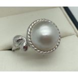 A modern design silver dress ring set with a single white Mabe pearl. Simple floral design to one