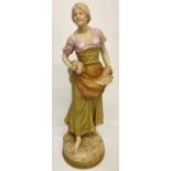 A large Royal Dux porcelain figure of a young girl in traditional dress carrying wheat.