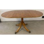 A modern reproduction satin wood veneer drop leaf table with pedestal base. Four metal claw feet…