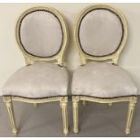 A pair of wooden framed balloon back style chairs, painted cream. With cream faux suede style