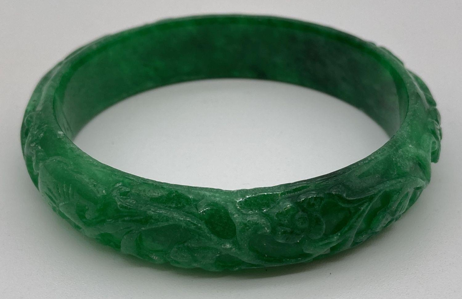 A green jade bangle with carved detail to outer surface. Approx. 7.5cm diameter.