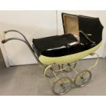 A vintage black and cream dolls pram by Tri-ang with rubber tyres, cloth hood and cover. Together