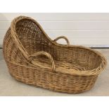 A vintage wicker baby Moses basket with carry handles.
