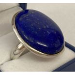 A modern silver statement dress ring set with a large oval lapis lazuli stone.