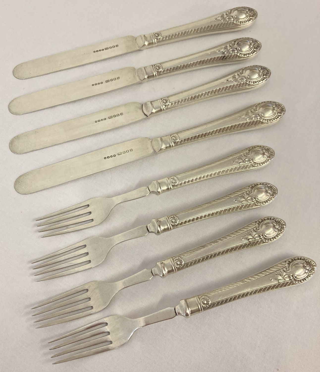 A set of 4 antique white metal knives and forks with floral and shell decoration to handles.