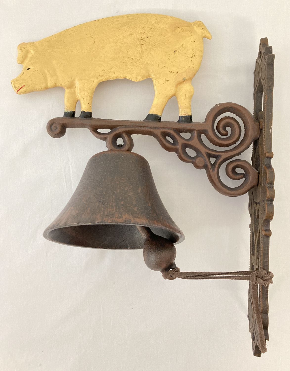 A painted cast metal wall hanging garden bell with pig design.