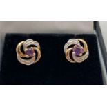 A pair of 9ct gold swirl design stud earrings set with central amethyst stones. Complete with