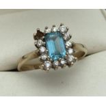 A 9ct gold blue topaz and clear stone dress ring. A square cut central blue topaz surrounded by
