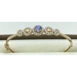 A 14ct gold hinged bangle with stone set flower design to top. Central oval iolite stone
