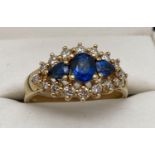 An 18ct gold, sapphire and diamond cluster style dress ring. Central oval cut sapphire with a