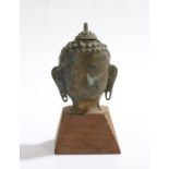 Tibetan cast metal Buddha head, mounted on a tapering wooden base, 17cm high