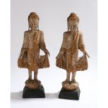 Pair of carved wooden standing buddha figures, with gilt decoration, raised on tapering black bases,