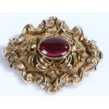 19th Century brooch, with a central cabochon garnet and scroll surround, 43mm diameter