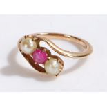 Gold coloured metal ring set with a red stone flanked by two pearls in a cross-over style setting,