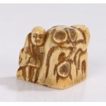 Japanese Edo period ivory Netsuke, with a figure near a rock and flowers, 35mm diameter, 30mm high