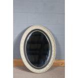 19th Century cream painted and ebonised oval wall mirror, the carved foliate frame, with ebonised