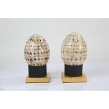 Pair of carved and decorated segmented bone eggs, on black and gilt stands, 22cm high