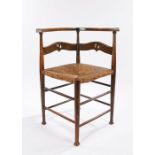 Arts and Crafts corner chair, the curved cresting rail above a pierced splat back and cane seat,