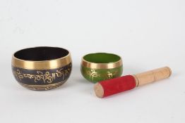 Two Tibetan musical bowls, each with script, with one beater, 11cm and 8cm diameter (3)