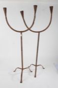 Pair of eastern metal floor standing candelabra, each having twin branches and raised on three feet,