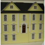 Large yellow painted wooden dolls house, 20th century, having hinged doors and roof with various