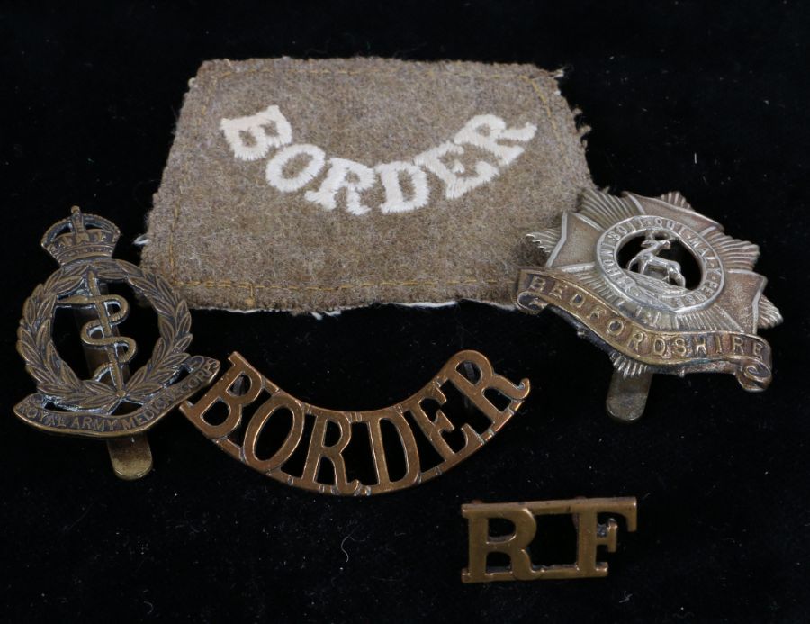 First World War cloth slip on shoulder title to the Border Regiment, together with cap badges to the