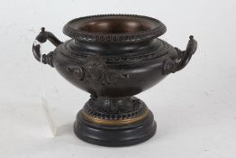 Bronze pedestal bowl, with beaded rim above a bulbous mask decorated twin handled body, raised on