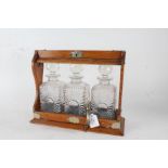 Edwardian electro plate mounted oak tantalus, containing three clear glass decanters with