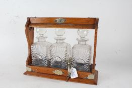 Edwardian electro plate mounted oak tantalus, containing three clear glass decanters with