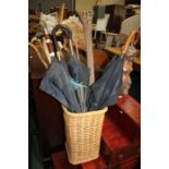 Wicker stick stand with a collection of various walking sticks and umbrellas etc. (qty)