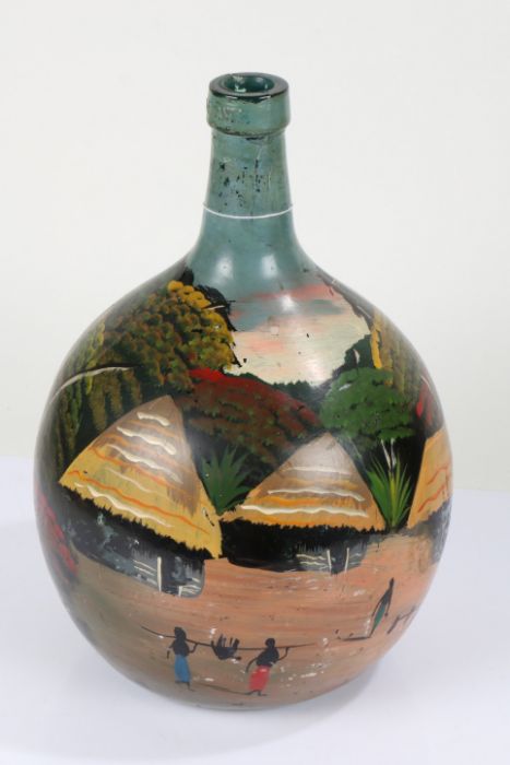 Nigerian painted green glass demijohn, decorated with houses in a forest, with figures besides a