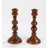 Pair of yew wood treen candlesticks, the turned sticks raised on rounded lead weighted bases, 22cm