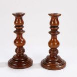 Pair of yew wood treen candlesticks, the turned sticks raised on rounded lead weighted bases, 21cm