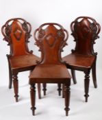 Three Victorian mahogany hall chairs, the pierced scroll carved cresting rails above shield carved