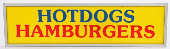 Yellow plastic panel inscribed "HOTDOGS HAMBURGERS" in blue and red, housed in an aluminium frame,