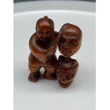 A Japanese hand carved netsuke of a gentleman selling Oni masks. Signed. [4.5cm in height]