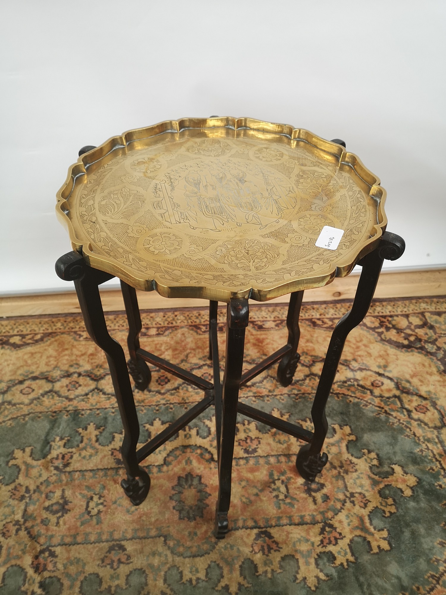 A brass tea tray table with scalloped edging, engraved in a Japanese theme, supported on a 6 arm/leg